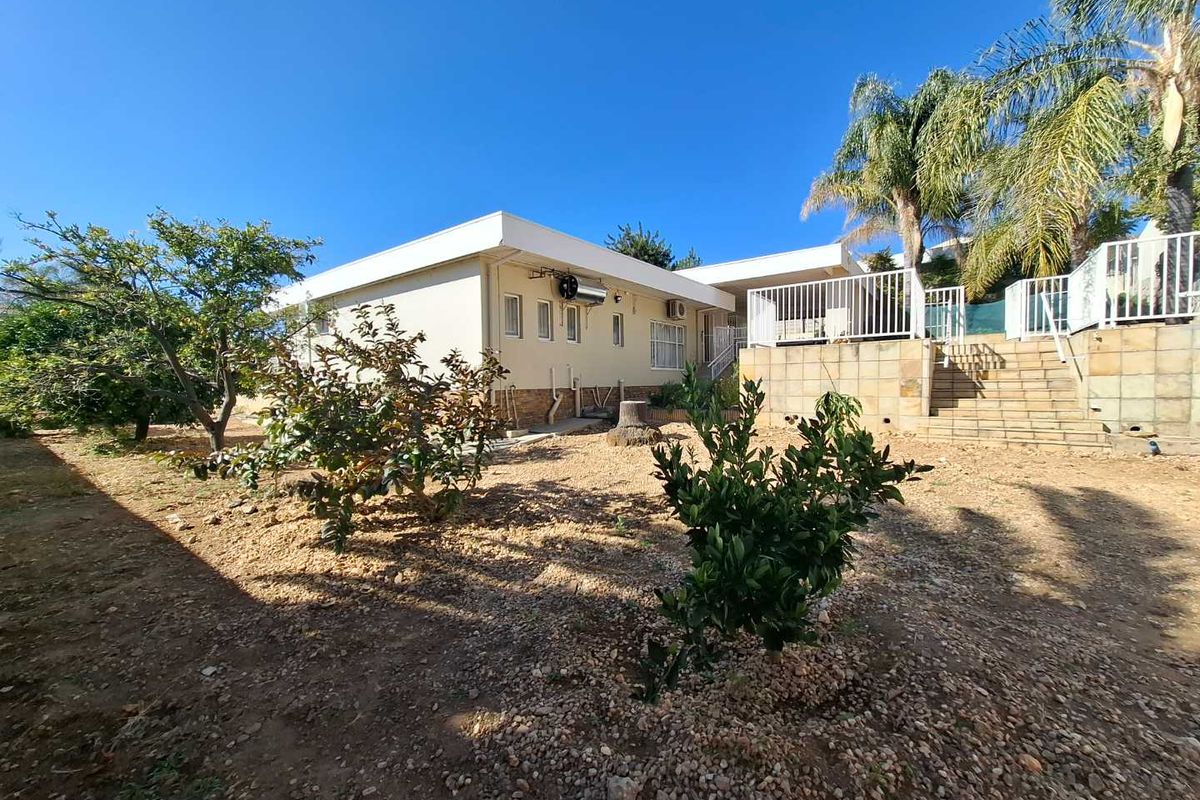 Rear view of the property featuring a garden area, retaining wall with staircase, and exterior access to the building structure.