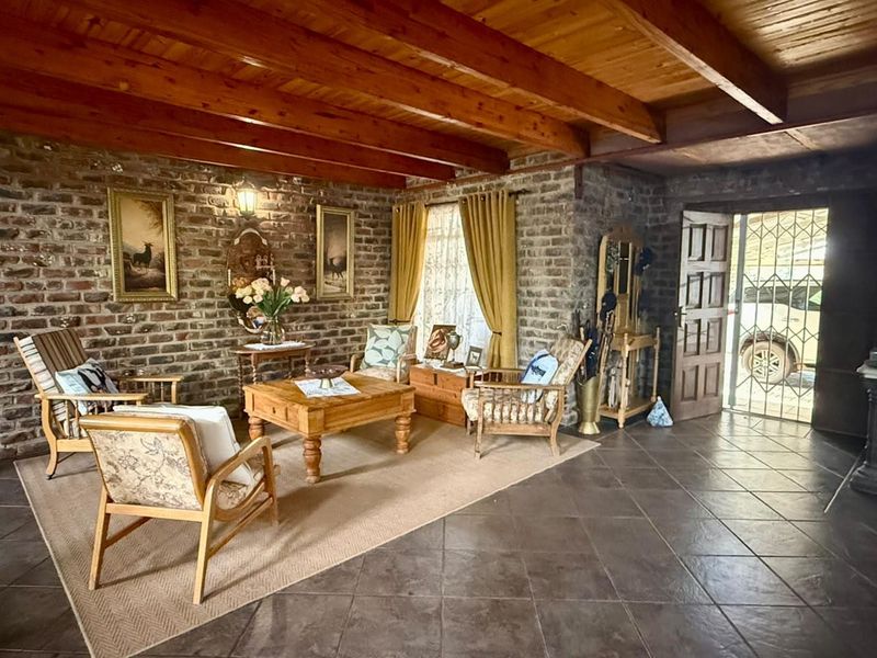 Rustic living room featuring exposed brick walls, timber beam ceiling, and tiled flooring, with direct access to the exterior through a security gate.
