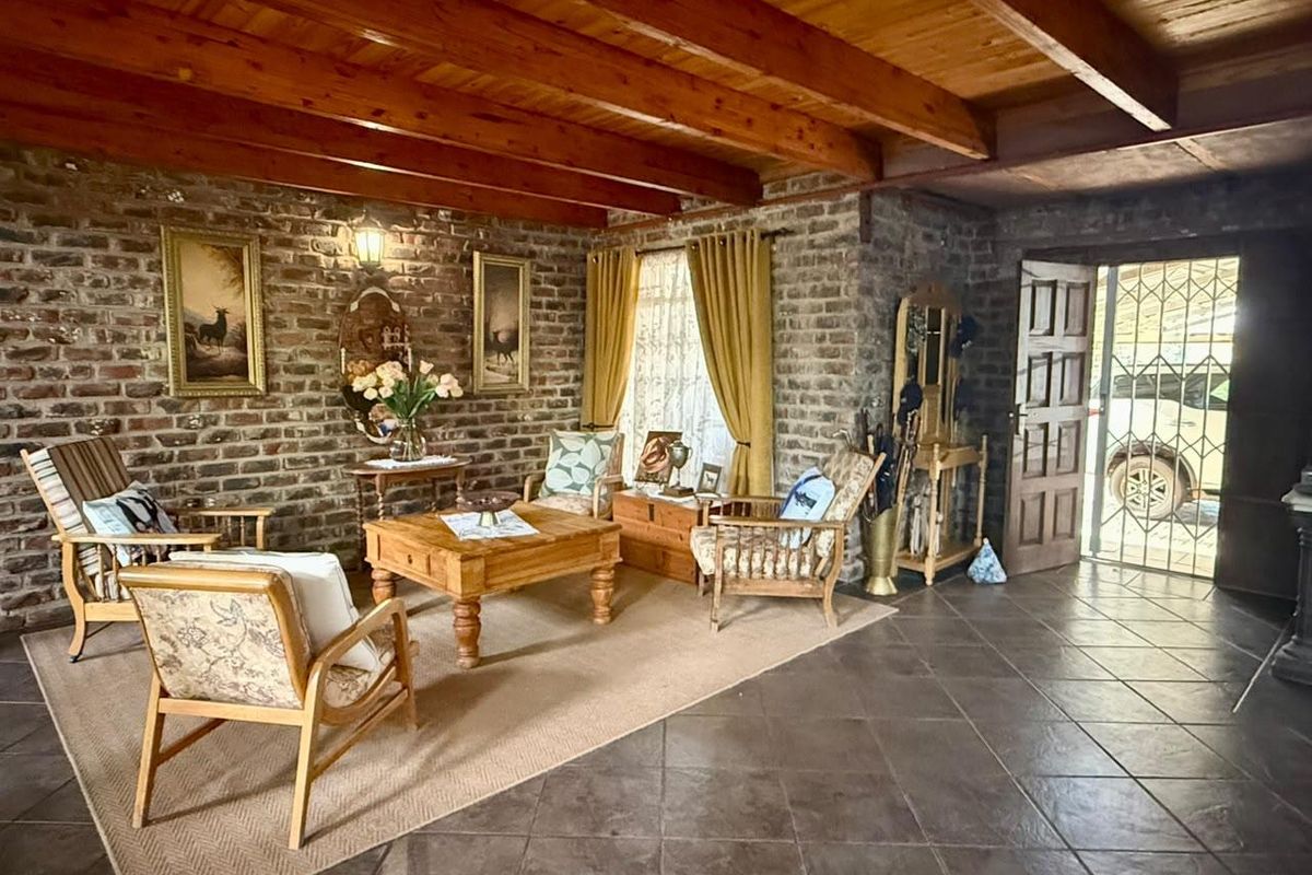 Rustic living room featuring exposed brick walls, timber beam ceiling, and tiled flooring, with direct access to the exterior through a security gate.