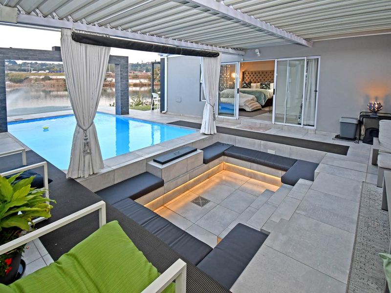 A luxurious outdoor entertainment area featuring a sunken seating pit with integrated lighting, a swimming pool, and a covered patio overlooking the water.