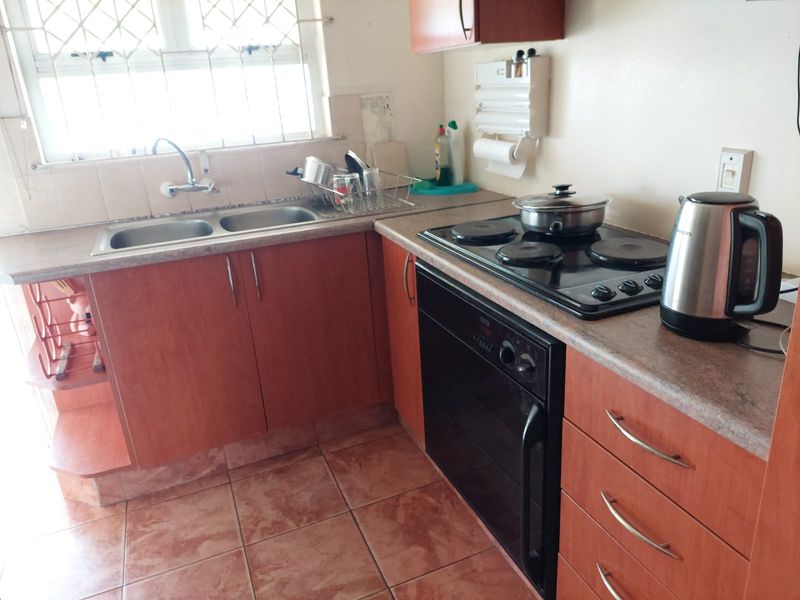 A compact kitchen featuring laminate countertops, a double basin sink, built-in oven, electric hob, and tiled flooring with some visible wear.