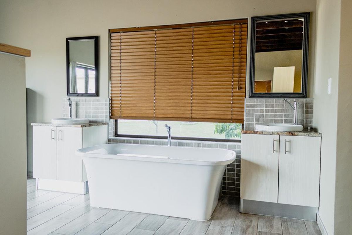 A modern bathroom featuring a freestanding bathtub, dual vanity units with vessel sinks, tiled splashbacks, and wooden blinds.