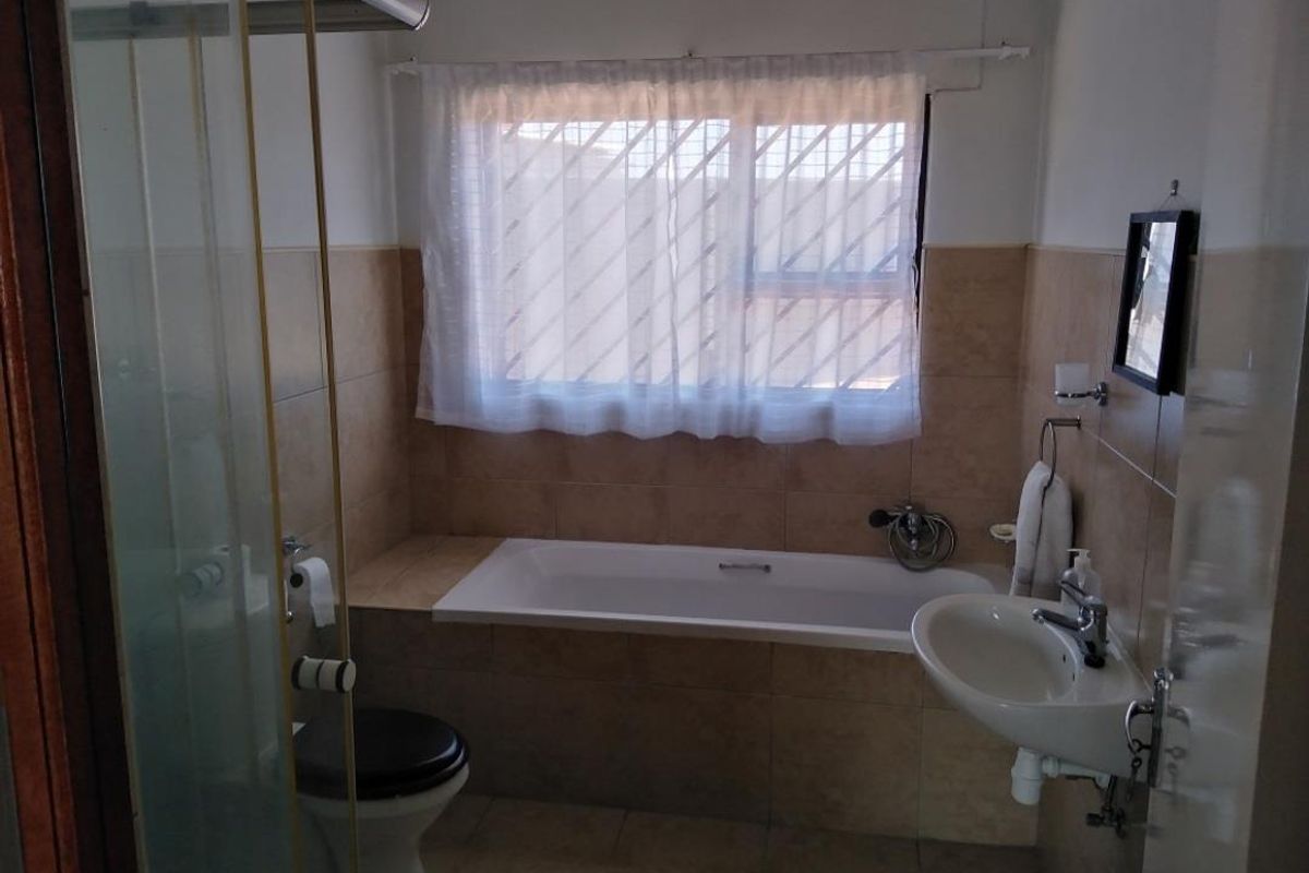 A functional bathroom featuring a built-in bathtub, a separate shower enclosure, a pedestal basin, and tiled walls.