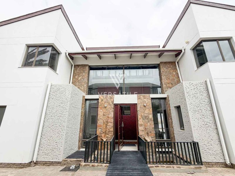 Modern double-storey residential facade featuring stone cladding, large glass windows, and a raised walkway leading to the main entrance.