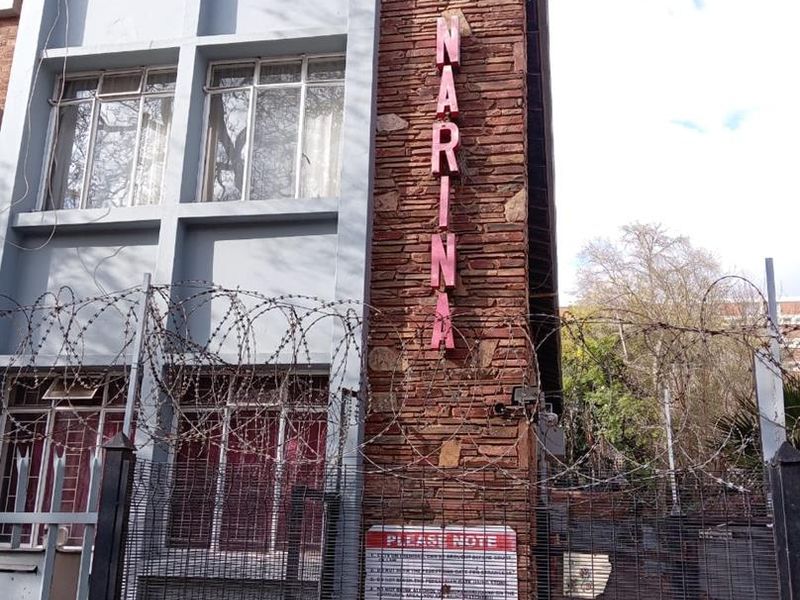 Exterior view of the apartment building facade featuring stone cladding, metal window frames, and security fencing with razor wire.