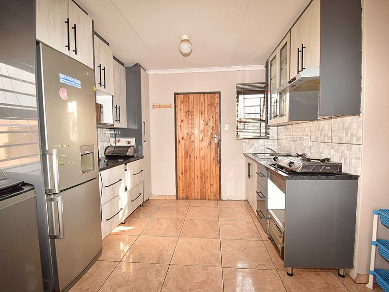 A functional kitchen featuring built-in cabinetry, gas hob, extractor fan, and tiled flooring, providing a practical workspace with direct access to an exterior door.
