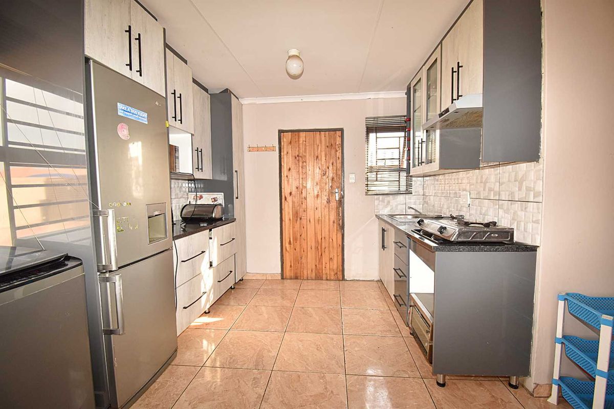 A functional kitchen featuring built-in cabinetry, gas hob, extractor fan, and tiled flooring, providing a practical workspace with direct access to an exterior door.