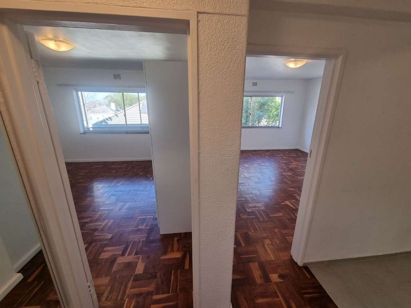 A view from the hallway looking into two empty bedrooms featuring original parquet flooring and large sliding windows.