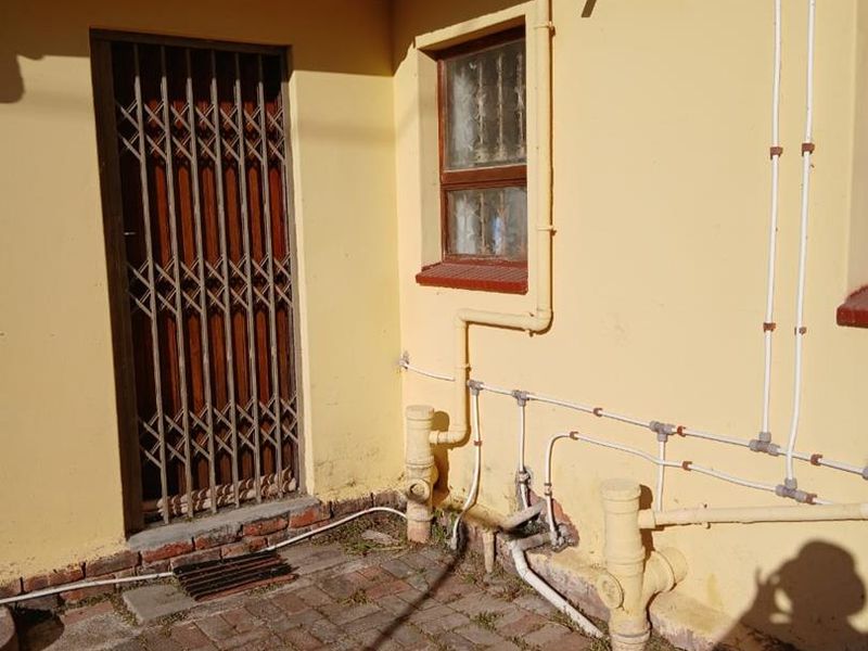 Rear exterior courtyard area featuring paved flooring, security gate access, and exposed exterior plumbing infrastructure.