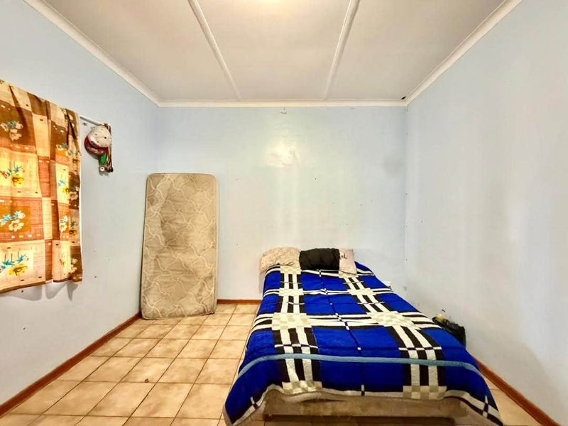 A simple bedroom featuring tiled flooring and a coved ceiling, currently requiring cosmetic updates to the wall finishes and flooring.