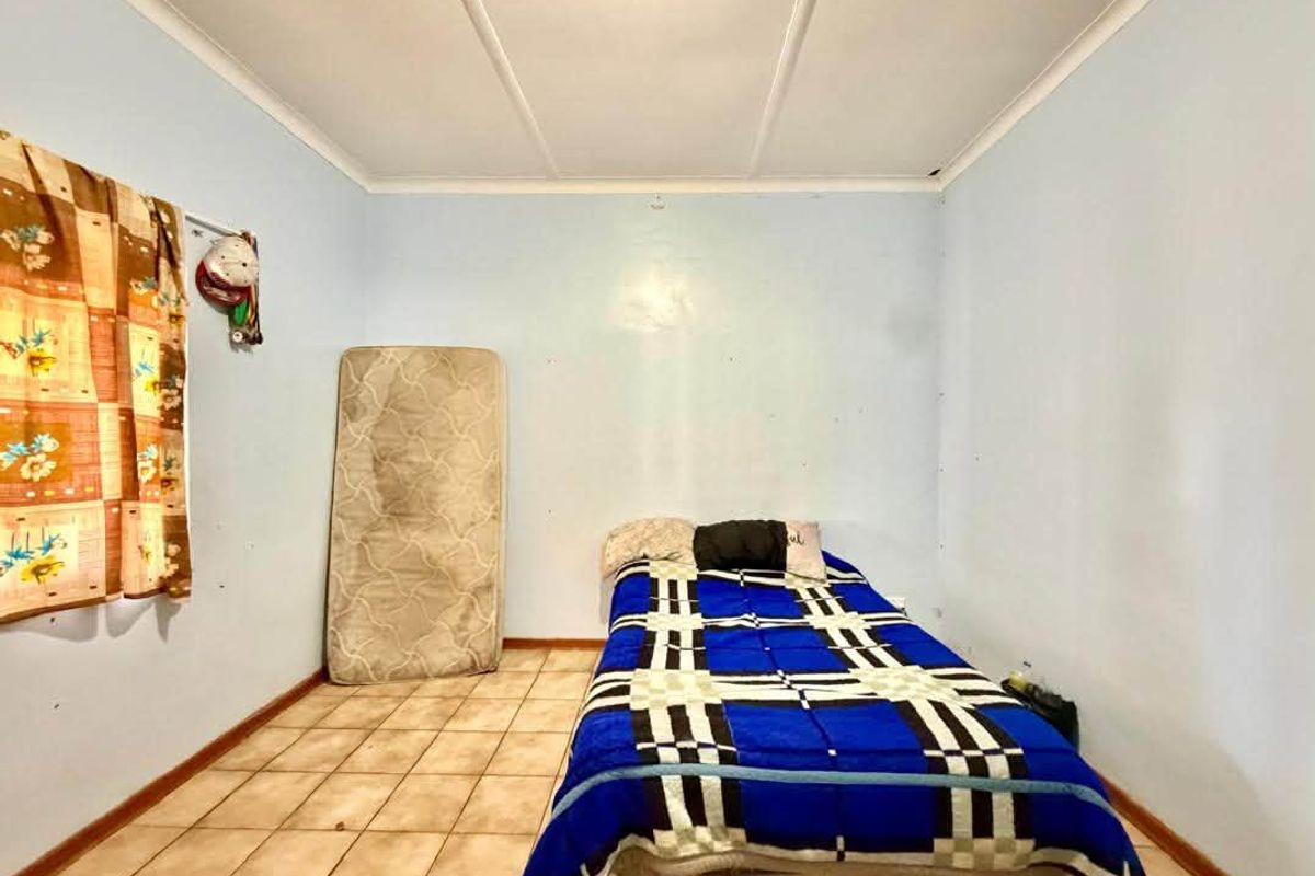 A simple bedroom featuring tiled flooring and a coved ceiling, currently requiring cosmetic updates to the wall finishes and flooring.