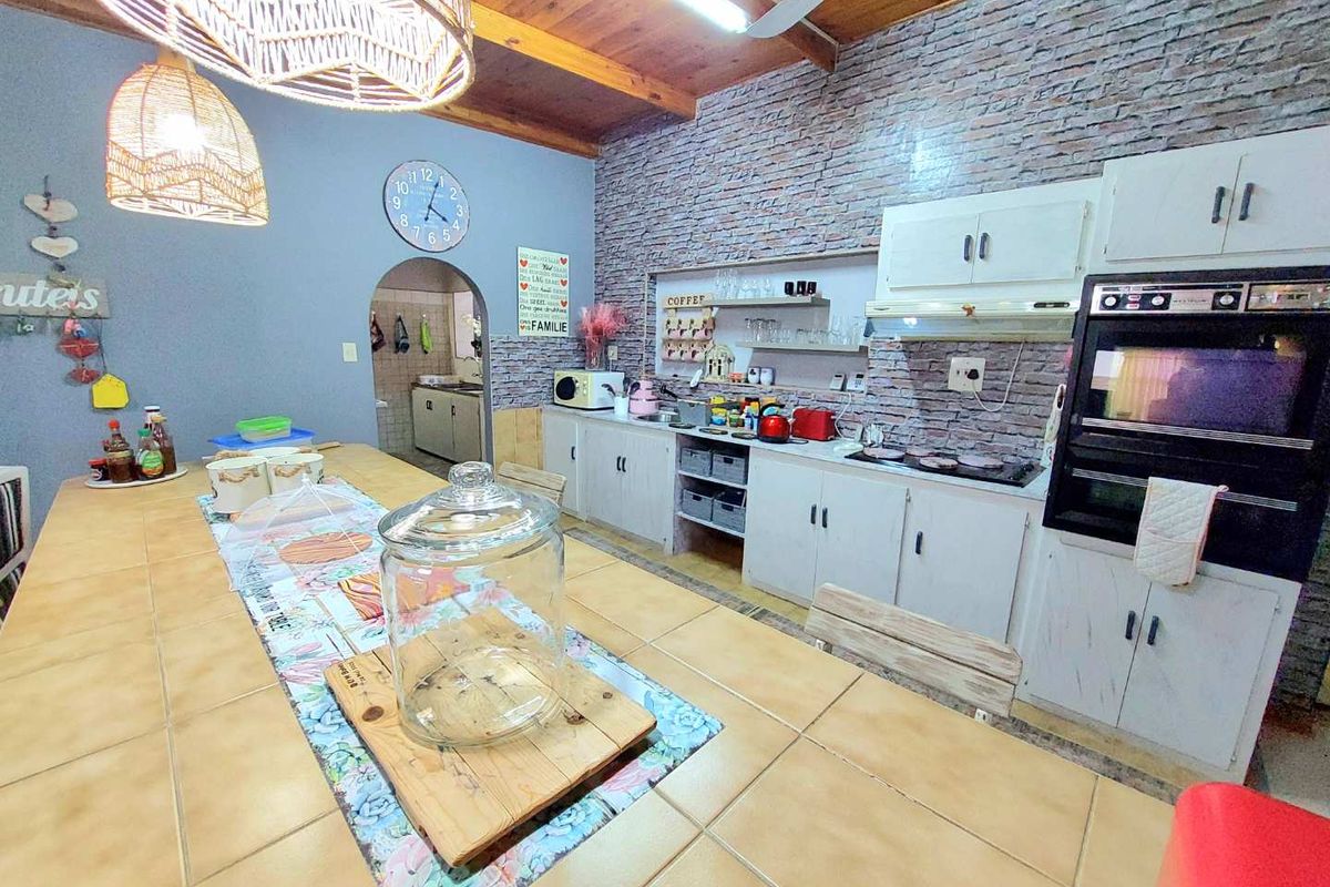 A rustic-style kitchen featuring a large tiled island, exposed timber ceiling beams, brick-cladding feature wall, and built-in oven with integrated cabinetry.