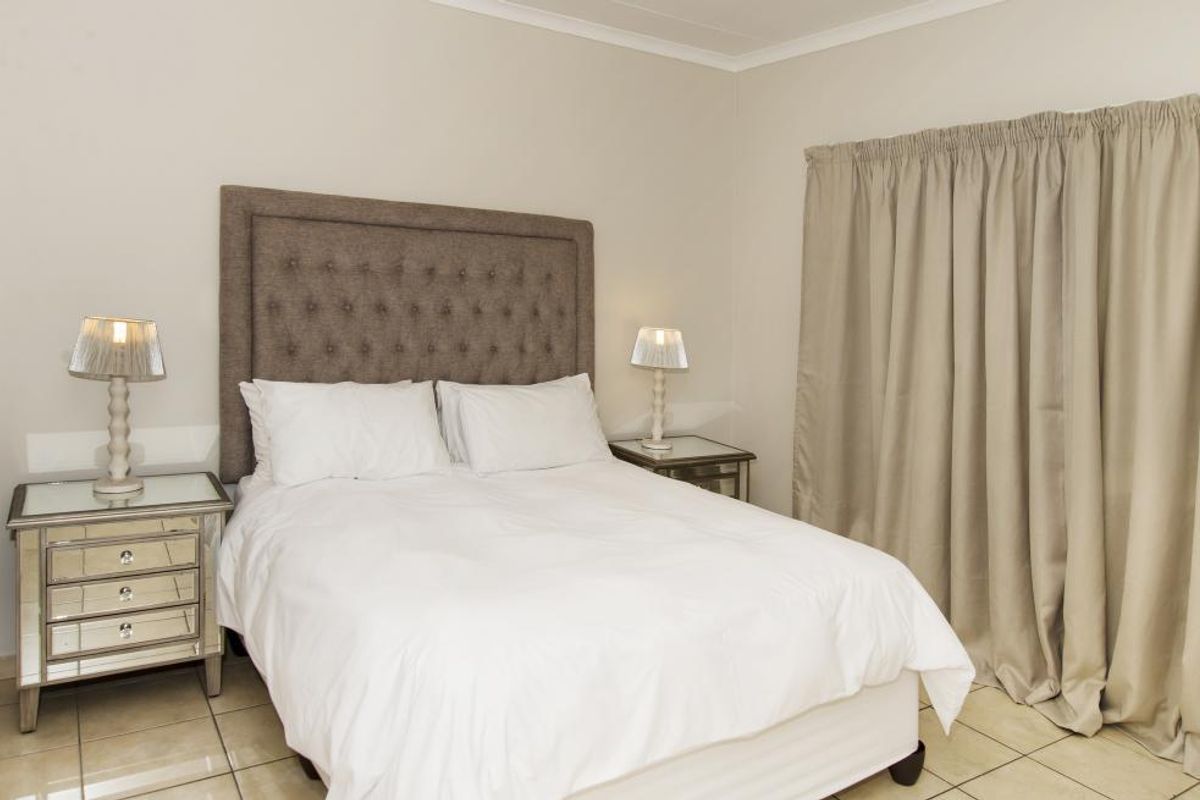 A well-lit bedroom featuring neutral wall tones, tiled flooring, and floor-to-ceiling curtains.