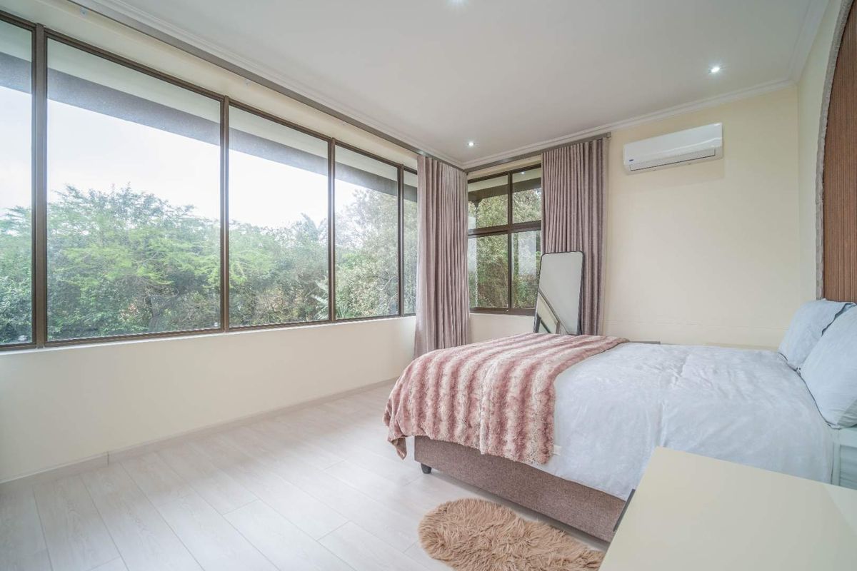 Bright and spacious bedroom featuring large floor-to-ceiling windows, light wood-look flooring, and a wall-mounted air conditioning unit.