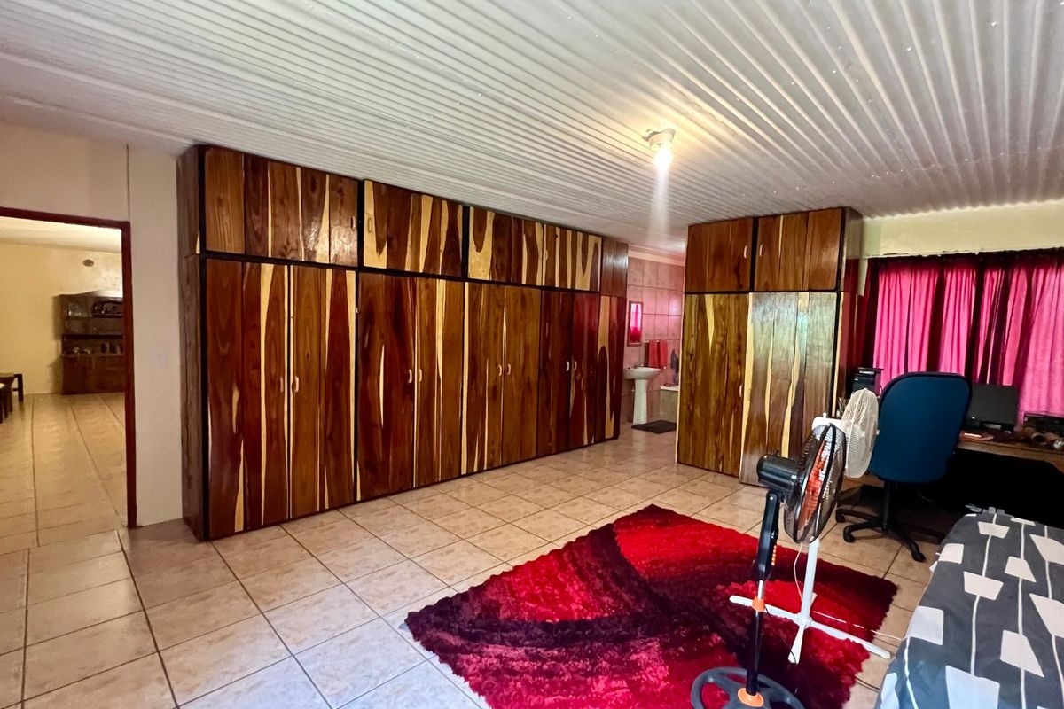 Spacious bedroom featuring extensive built-in wooden cabinetry, tiled flooring, and a corrugated ceiling, with direct access to an en-suite bathroom.
