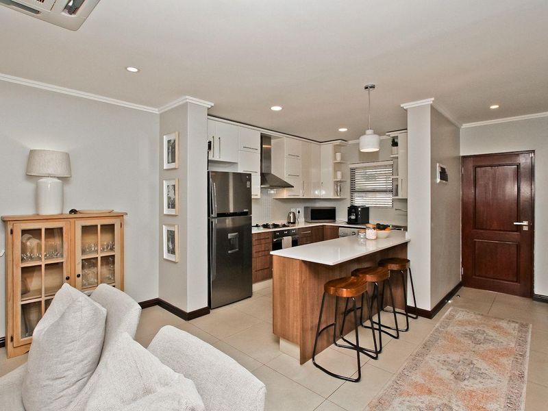 Modern open-plan kitchen featuring sleek cabinetry, stone countertops, a breakfast bar, and integrated appliances, seamlessly flowing into the living area.