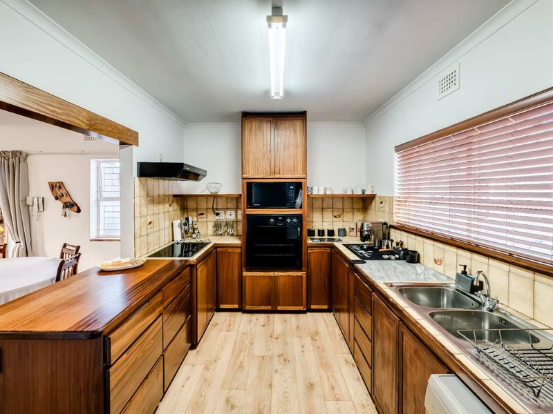 A functional kitchen featuring warm-toned wooden cabinetry, built-in appliances, a double stainless steel sink, and a tiled splashback with laminate flooring.