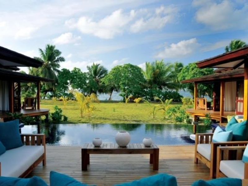 A stunning outdoor patio area featuring timber decking, overlooking a private swimming pool and lush tropical garden with ocean views.
