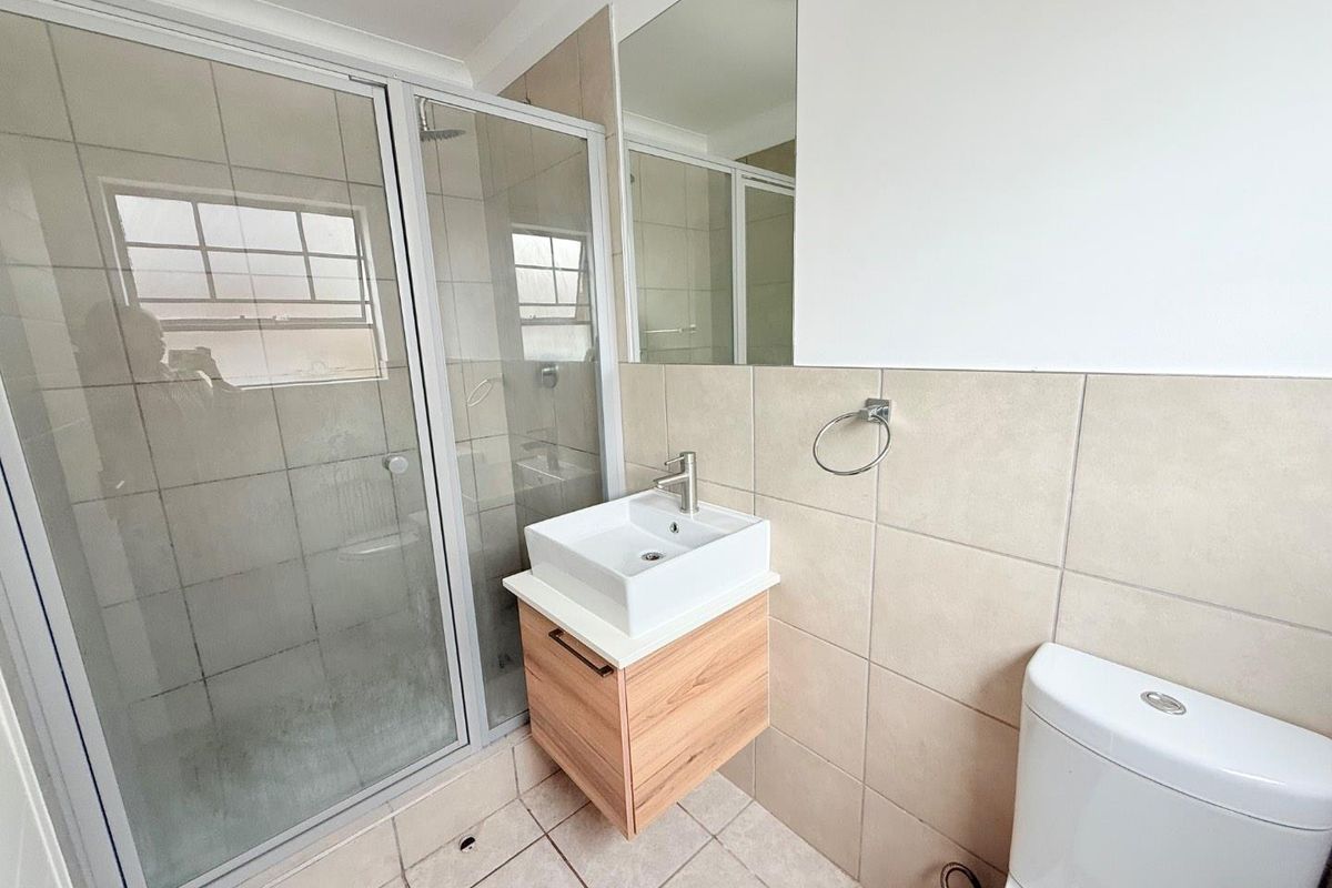 A functional bathroom featuring a glass-enclosed shower, a modern wall-mounted vanity with a vessel sink, and a standard toilet.