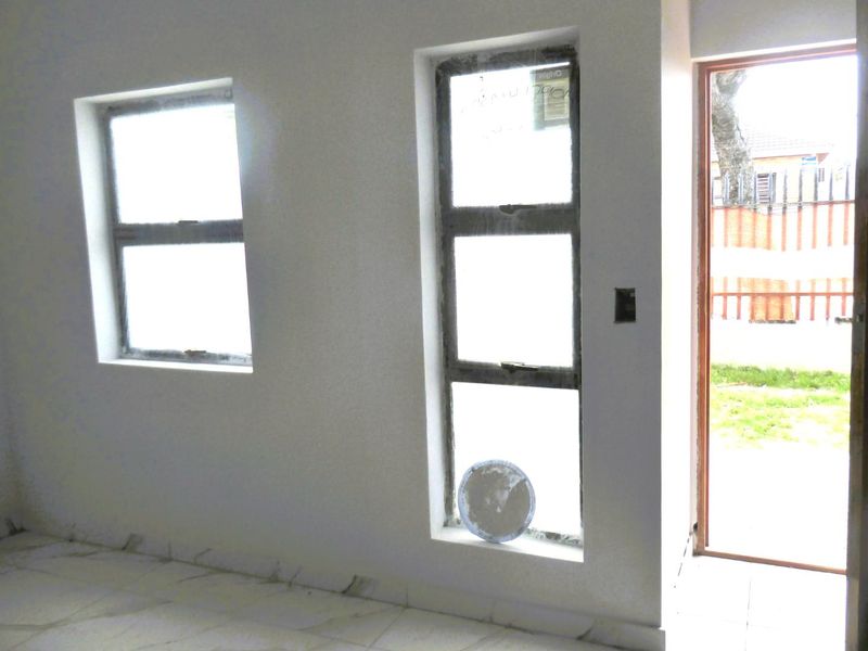 An empty living area featuring tiled flooring, aluminium windows, and direct access to the exterior, currently in an unfinished state.