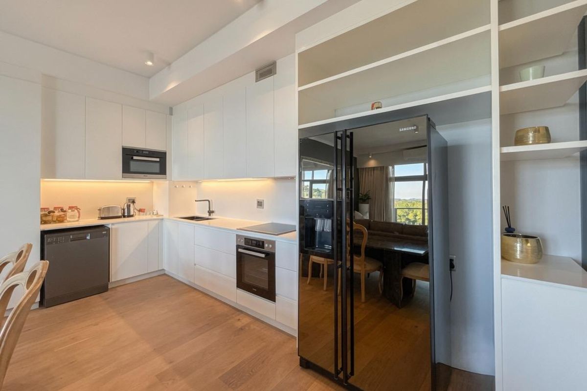 Modern kitchen featuring sleek white cabinetry, integrated appliances, under-cabinet lighting, and high-quality timber flooring in an open-plan layout.