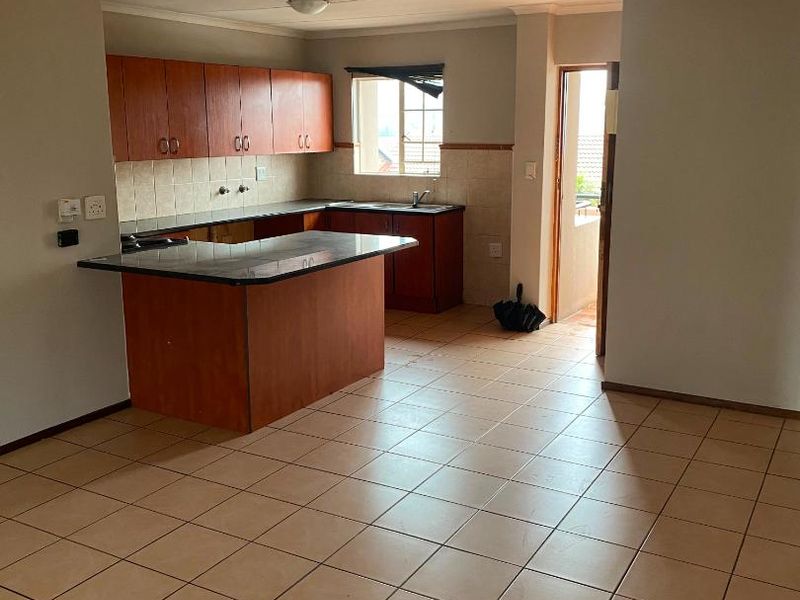 An open-plan kitchen and living area featuring tiled flooring, wooden cabinetry, granite countertops, and direct access to an outdoor balcony.