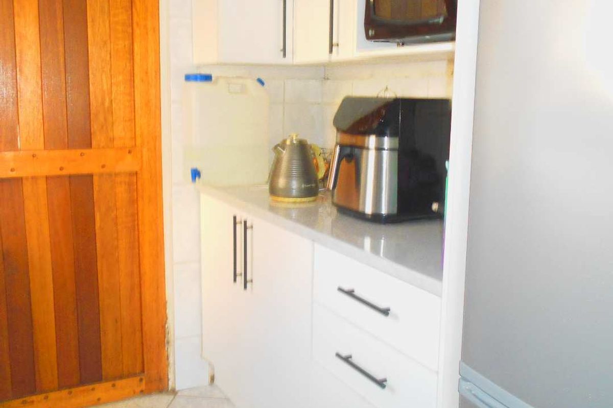 A compact kitchen area featuring white built-in cabinetry, stone countertops, and tiled flooring, adjacent to a wooden door.
