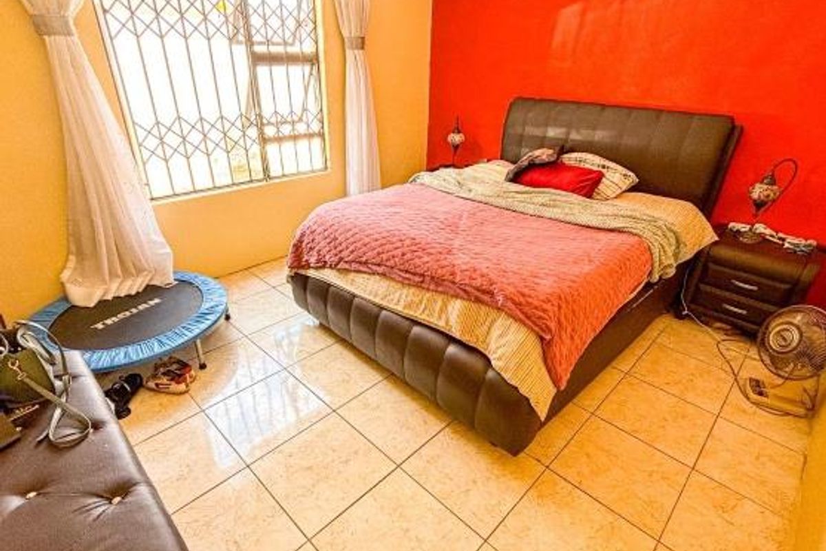 A bedroom featuring tiled flooring, a large window with security bars, and a bold red accent wall.