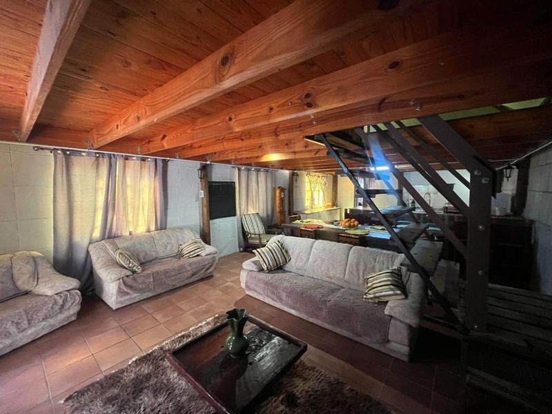 Open plan living and kitchen area featuring exposed timber ceiling beams, tiled flooring, and a central metal staircase.