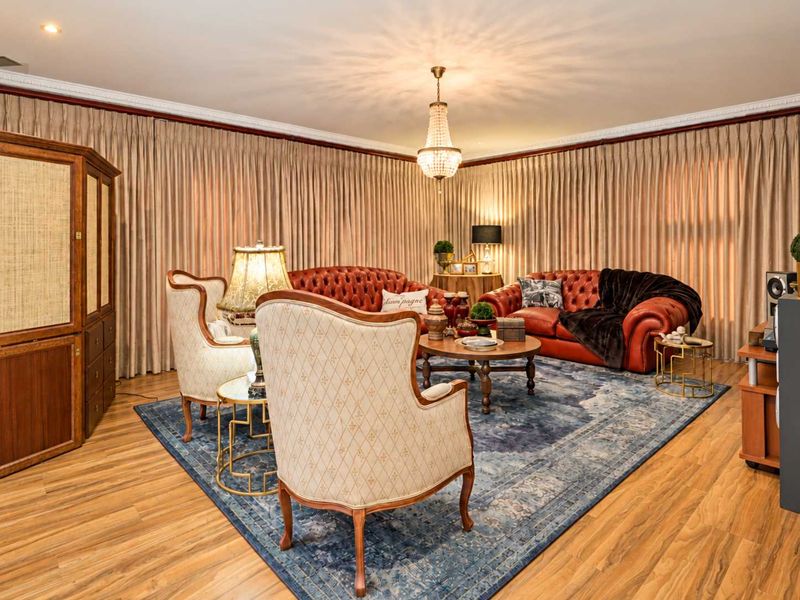 A formal living room featuring laminate flooring, decorative coving, recessed downlights, and a central crystal chandelier.