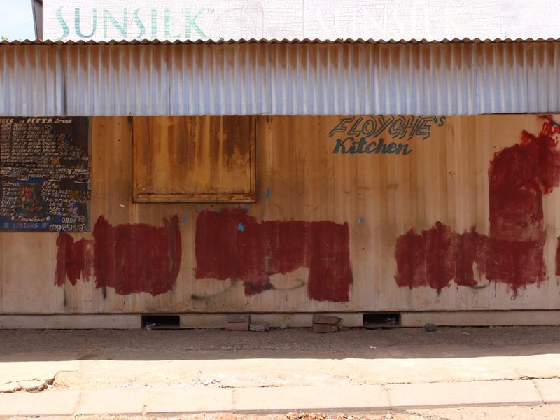 A commercial shipping container structure featuring a corrugated metal roof and a service window, currently used as a food service kiosk.
