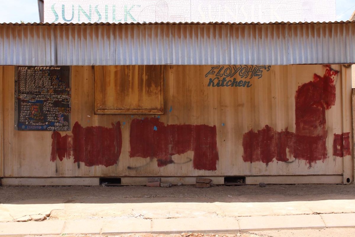 A commercial shipping container structure featuring a corrugated metal roof and a service window, currently used as a food service kiosk.