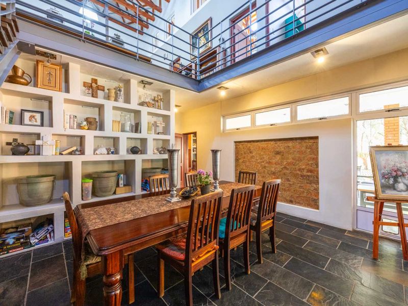 Spacious dining area featuring slate flooring, an exposed brick accent wall, built-in shelving, and an open mezzanine level with a metal staircase.