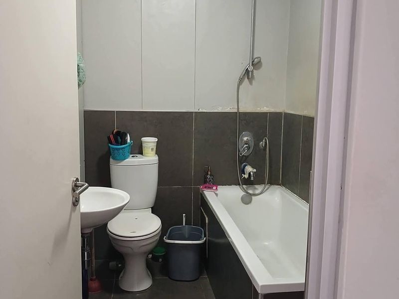 Compact bathroom featuring a pedestal basin, toilet, and a bathtub with a handheld shower mixer, finished with dark floor and wall tiles.
