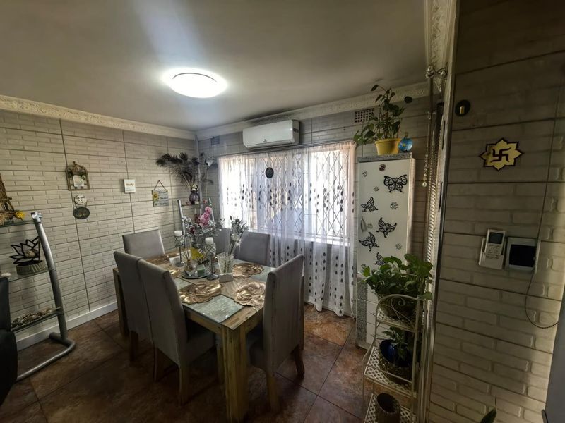 A dining room featuring brick-style wall cladding, tiled flooring, decorative ceiling cornices, and a wall-mounted split-system air conditioner.