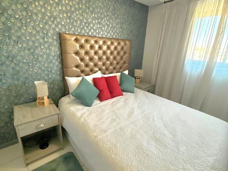 A well-maintained bedroom featuring a decorative patterned feature wall, neutral tiled flooring, and natural light through window curtains.