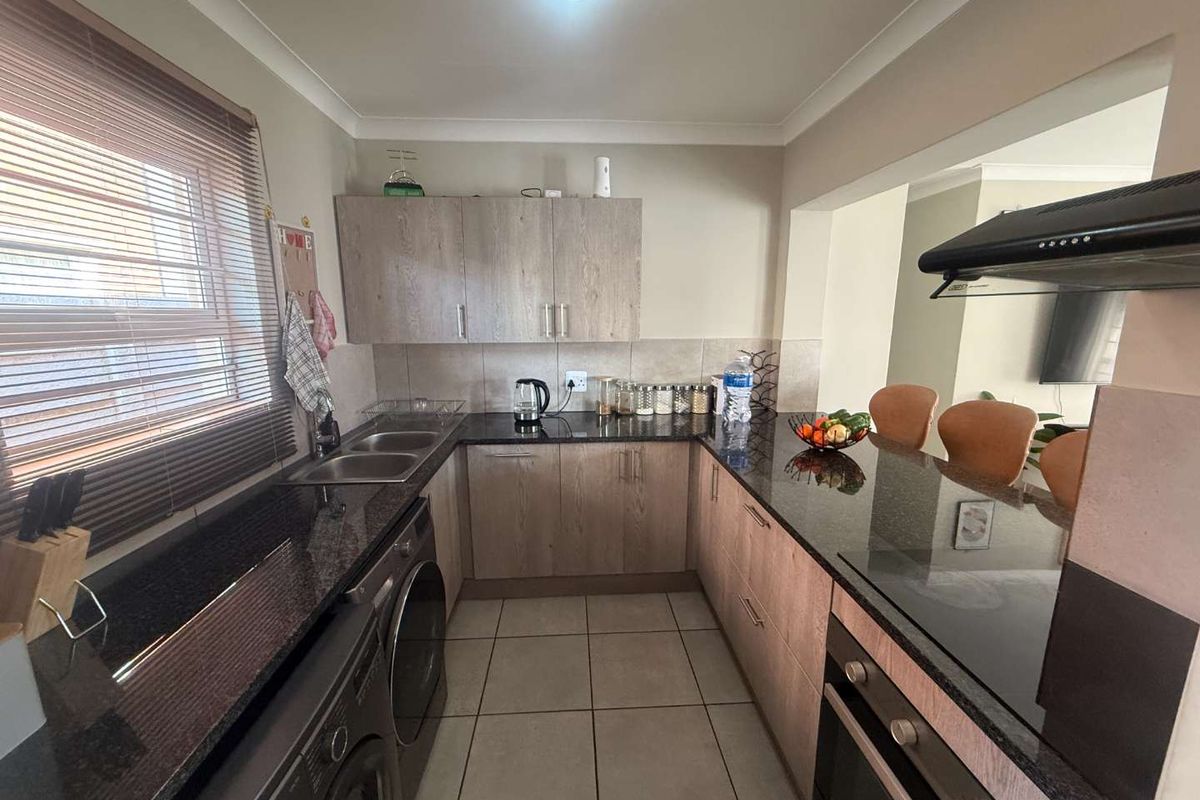 A functional kitchen featuring granite countertops, built-in cabinetry, a hob with extractor fan, and an integrated oven, with tiled flooring throughout.