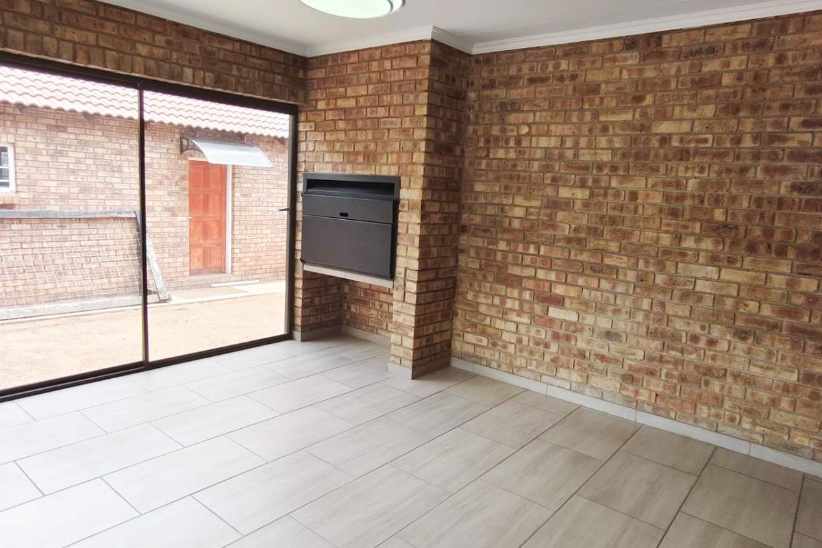 A bright living area featuring exposed brick walls, modern light-colored floor tiles, and a built-in fireplace, with sliding glass doors leading to the exterior.