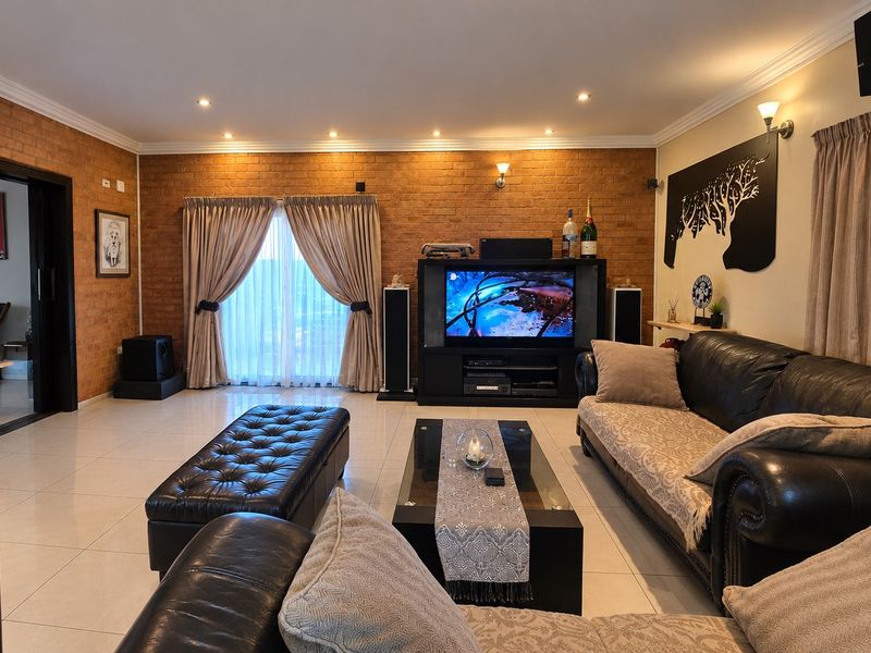 Spacious living room featuring an exposed brick feature wall, tiled flooring, and recessed downlighting, creating a warm and inviting atmosphere.