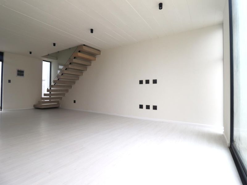 A bright, modern, and spacious open-plan living area featuring a contemporary floating staircase, sleek laminate flooring, and large glass doors providing ample natural light.