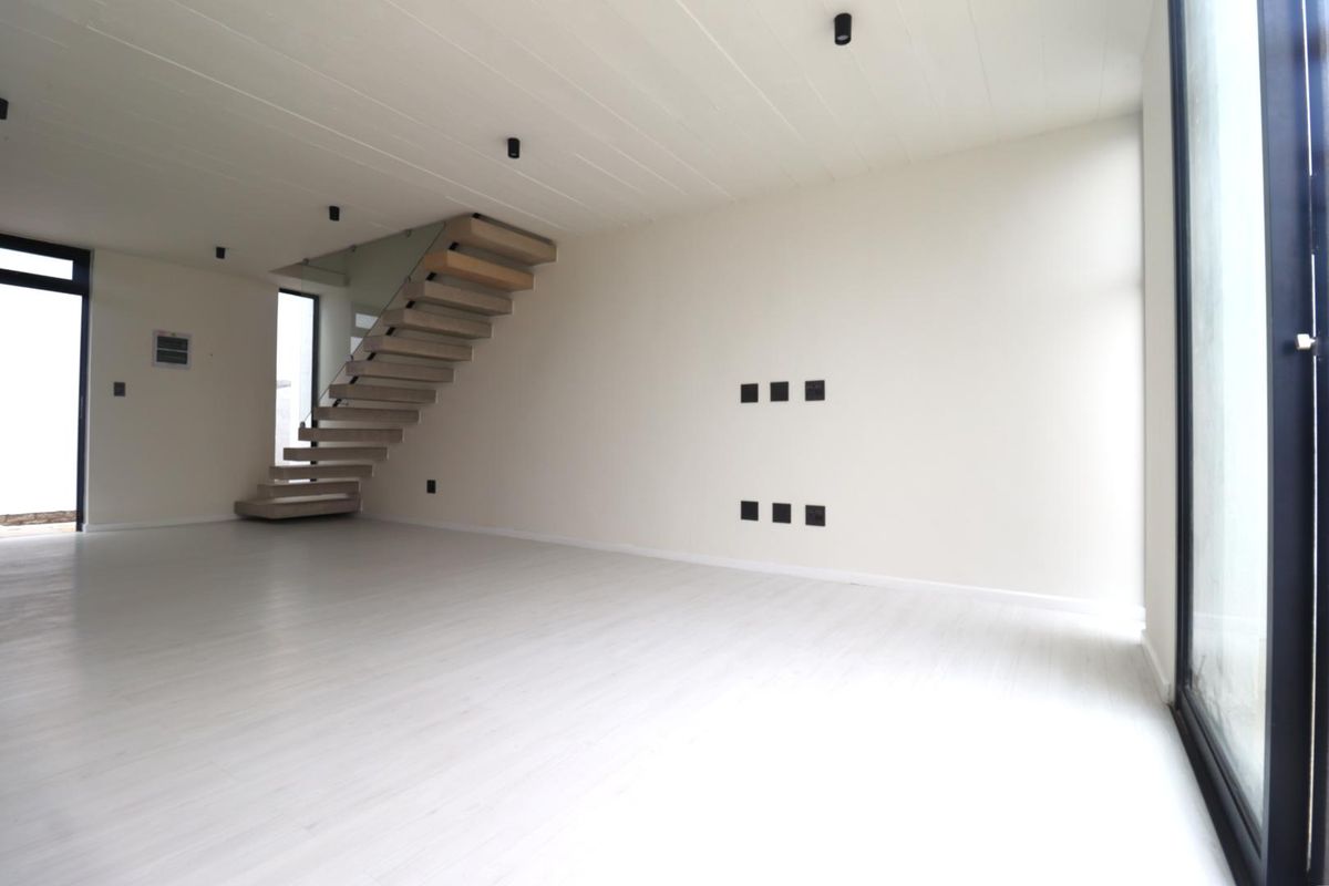 A bright, modern, and spacious open-plan living area featuring a contemporary floating staircase, sleek laminate flooring, and large glass doors providing ample natural light.
