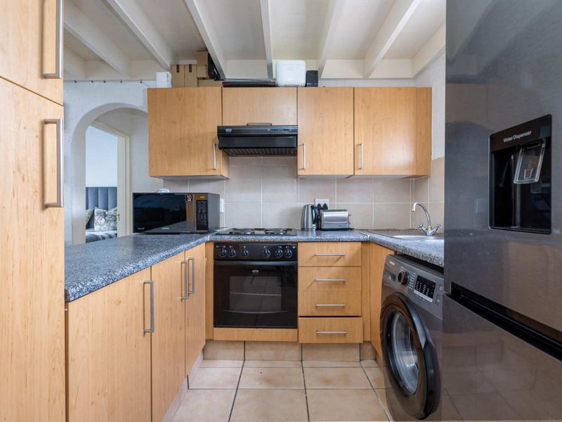 Compact kitchen featuring light wood cabinetry, granite-look laminate countertops, built-in oven with extractor fan, and tiled flooring with exposed beam ceiling detail.