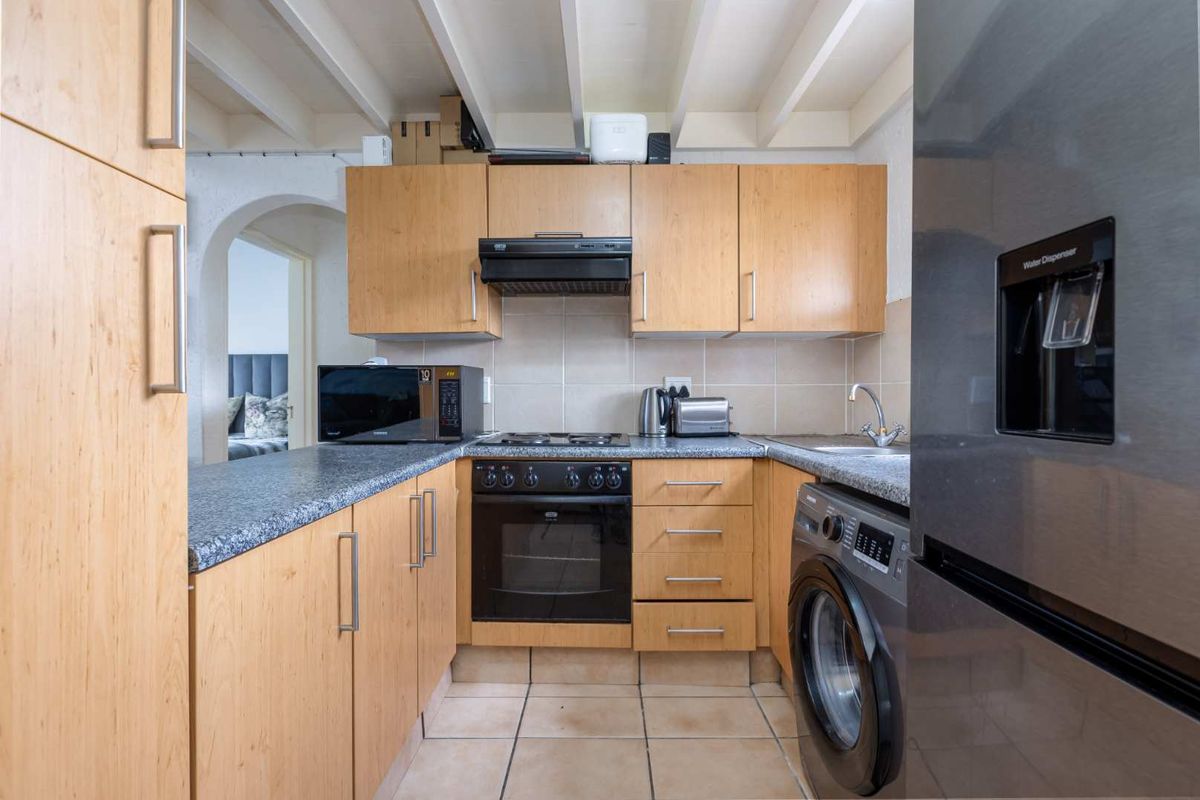 Compact kitchen featuring light wood cabinetry, granite-look laminate countertops, built-in oven with extractor fan, and tiled flooring with exposed beam ceiling detail.