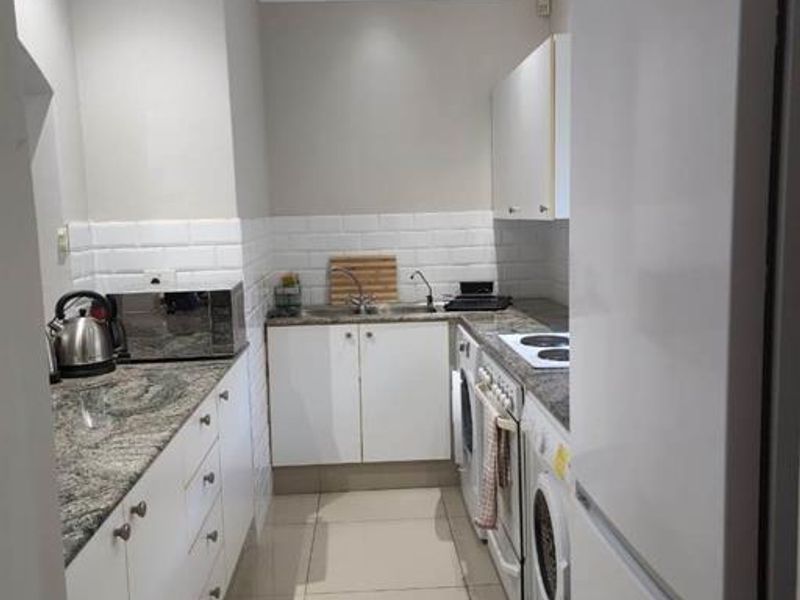 A compact, functional kitchen featuring granite countertops, white cabinetry, subway tile backsplash, and integrated appliances including an oven and hob.