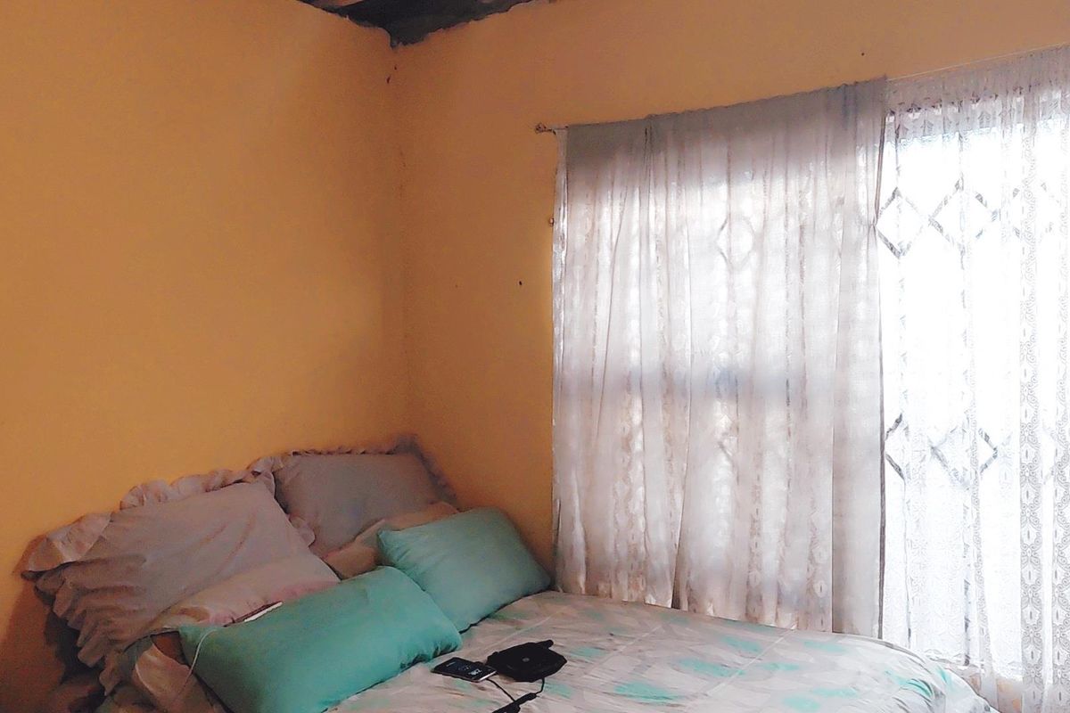 A bedroom featuring a window with a security gate, showing signs of wear on the walls and ceiling.