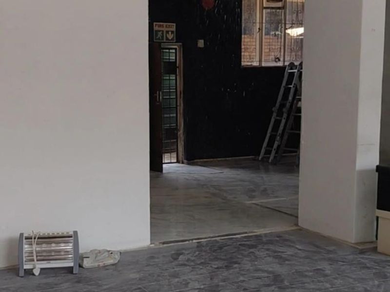 An empty office space featuring tiled flooring, a fire exit, and security-barred windows, currently requiring cosmetic updates and maintenance.