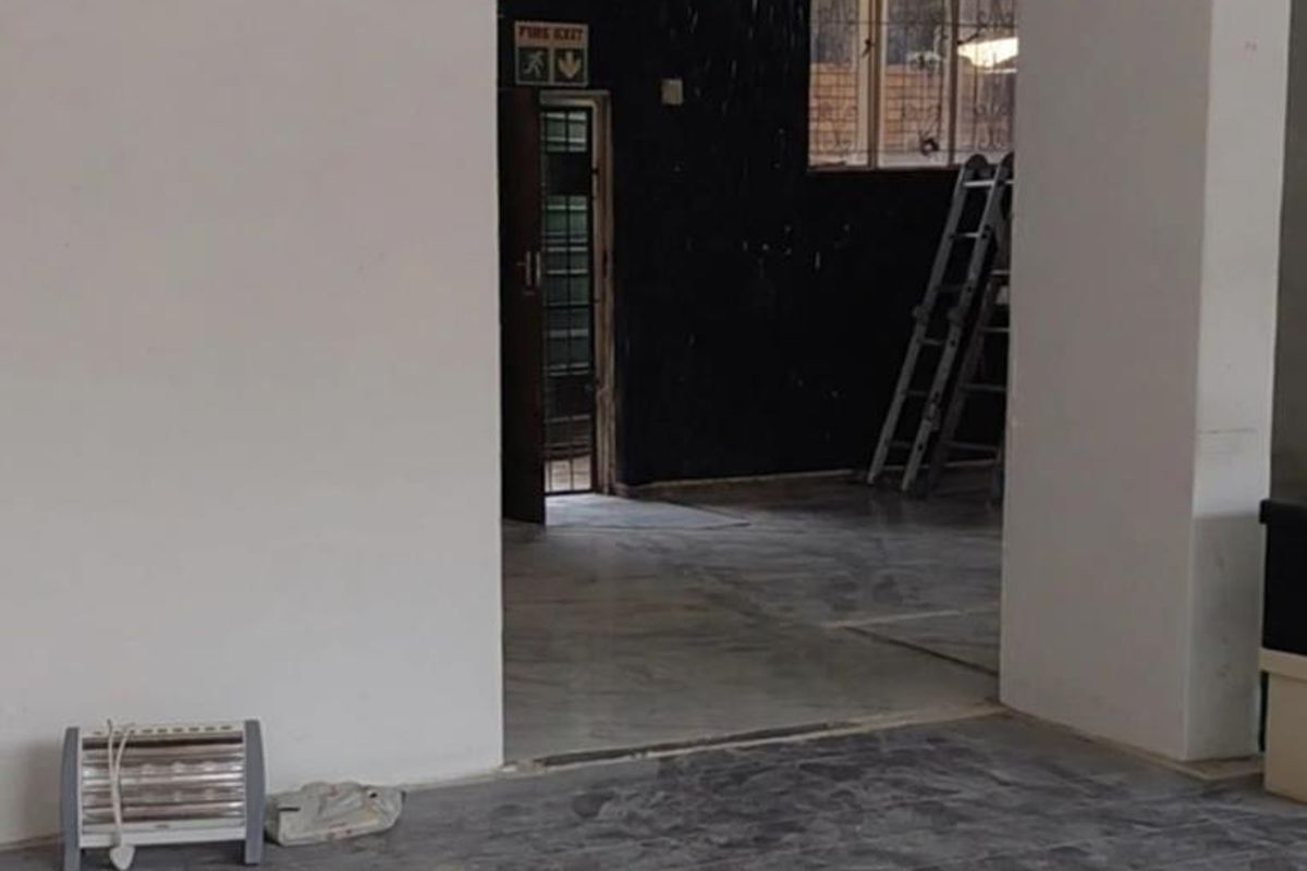 An empty office space featuring tiled flooring, a fire exit, and security-barred windows, currently requiring cosmetic updates and maintenance.