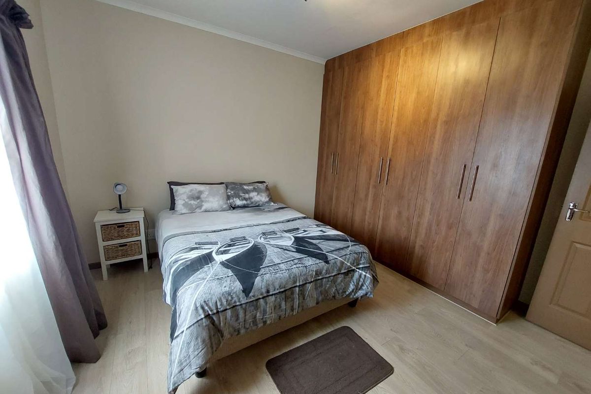 A well-maintained bedroom featuring light wood-look flooring and extensive floor-to-ceiling built-in wooden cabinetry for ample storage.