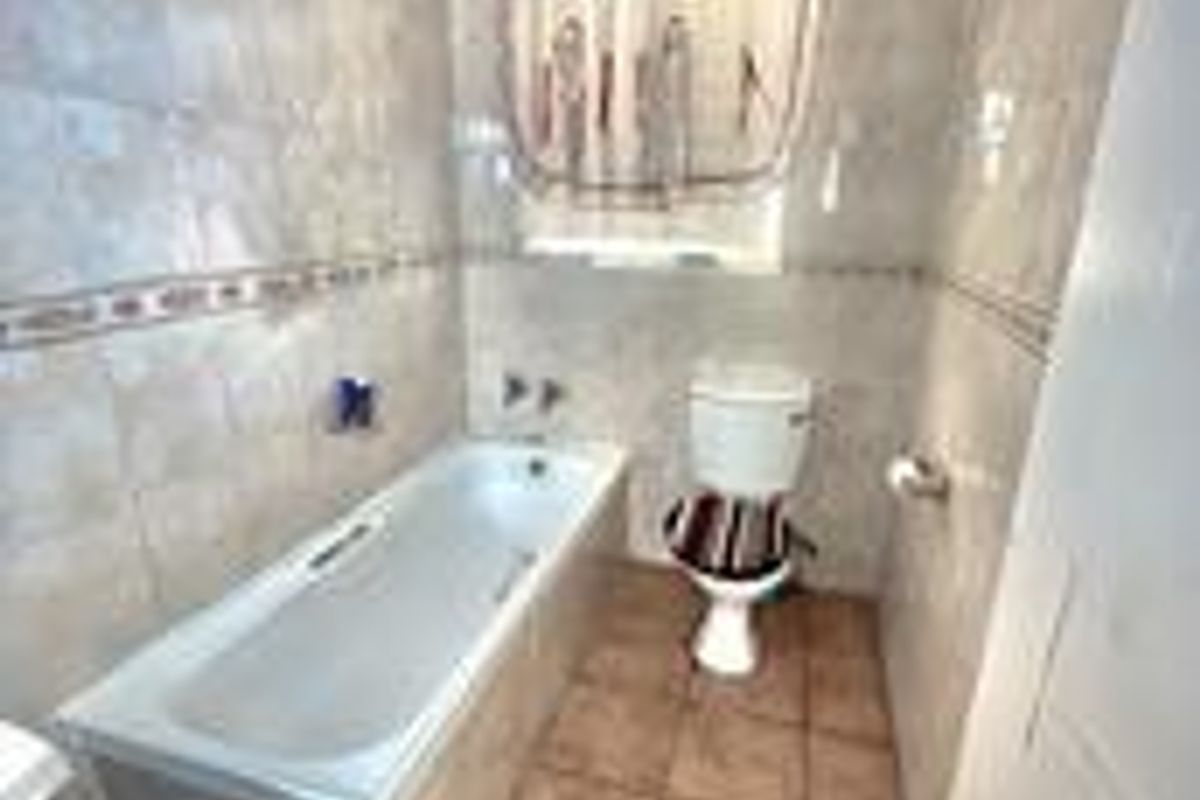 A functional bathroom featuring a bathtub, toilet, and neutral ceramic wall and floor tiling.