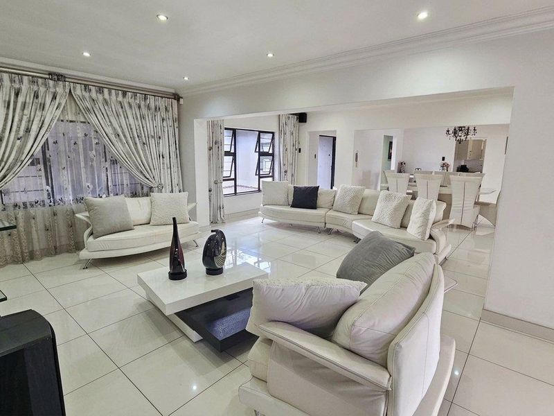 Spacious open-plan living and dining area featuring polished porcelain floor tiles, recessed downlighting, and large aluminium-framed windows.